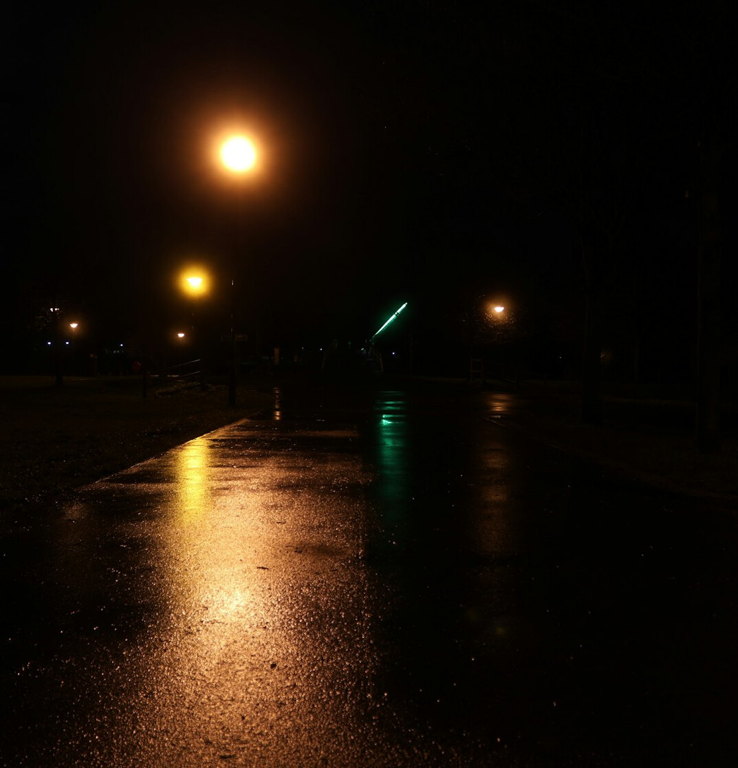 Rainy city street at night with glowing lamppost reflections